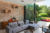 Living room with brick wall, grey corner sofa and garden view