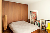 Double bed against wood-clad wall and artworks on floor leaning against white wall