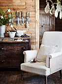 Light-coloured upholstered armchair in front of rustic chest of drawers
