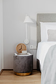 Bedside table and wall-mounted lamp next to bed with white bed linen