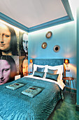 Petrol-blue bedroom with Mona Lisa wallpaper on wall next to bed