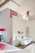 Freistehende Badewanne im offenen Schlafzimmer, rosa Treppe hinter Raumteiler