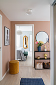 Sideboard below mirror on peach-coloured wall of hallway with view into bedroom