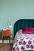 Double bed with patterned bedspread and bedside table against duck egg blue wall