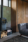 Log burner against concrete wall and grey sofa in open-plan interior