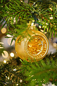 Golden Christmas bauble hanging from branch in front of twinkling lights