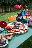 Brotzeitbrett mit Schinken, Salami und Weintrauben auf Tisch im Freien