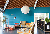 Wohnzimmer mit blauen Wänden, bunt gestreifter Couch und Holzdecke