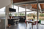 Open-plan kitchen and dining area with large window front, wooden ceiling and concrete wall