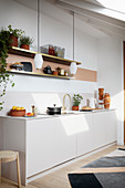A white kitchen counter with an open shelf above it and pendant lamps hanging from the ceiling