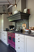 A pink oven in a classic grey kitchen with an extractor hood