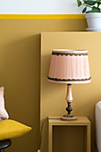 Old table lamp on bedside table against ochre wall with ledge