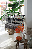 Autumnal arrangement on stool in front of hanging chair with scatter cushions