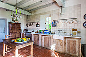Holztisch in rustikaler Küche mit Holzbalken und Terrakotta-Fliesenboden