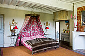 Double bed with fur blanket and red toile de jouy canopy in bedroom