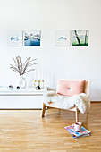 Magazines and cup next to wooden armchair with sheepskin rug and cushion in living room
