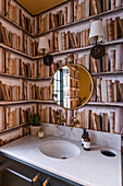 Washstand below round mirror and library-effect wallpaper