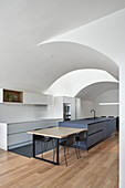Dining table next to island counter in modern kitchen with vaulted ceiling