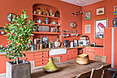 Landhausküche mit terrakottafarbenen Wänden, Holztisch und Tajine-Topf im Vordergrund