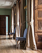 Upholstered chairs in the classic hallway with curtains at the window recesses