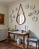 Plates with jester painted on them mounted on a wall encompassing a round hanging mirror above antique washstand