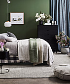 Double bed and dresser with lush bouquet of flowers in front of green wall