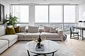 A beige corner sofa in front of a window in a living room with a panoramic view of the city