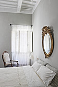 Gilt-framed mirror above double bed in bedroom with light grey walls