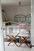 Folding stools at feet of twin green metal beds in vintage-style bedroom