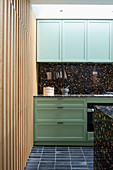 Black terrazzo elements, green cabinets and wood cladding in kitchen