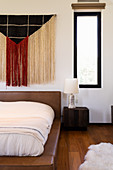 Fringed wall hanging above leather-upholstered bed