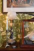 Antique table lamp and candlestick on wooden table against green wallpaper