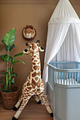 Zimmerpflanze und Giraffenfigur neben Babybett mit Baldachin