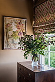 Bouquet of flowers on a chest of drawers and painting with floral motif in corner of room
