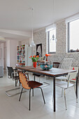 Dining area with various chairs in front of white painted brick wall in open plan living room