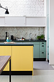 Kitchen island with yellow front in open-plan kitchen with white-painted brick wall