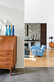 View past retro bureau into living room with light blue armchairs and stone wall
