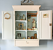 Collection of little, old bottles and vintage-style ornaments in wall-mounted cabinet