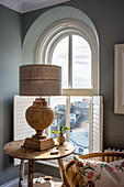 Table lamp on side table in front of arched window