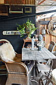 Wicker chair with sheepskin rug at wooden table on terrace with vintage-style accessories
