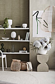 White shelves with decorative objects, modern art on the wall, concrete stool with bouquet of flowers in front of it