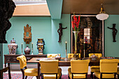Yellow leather chairs around dining table in front of carved wooden figures and artworks on wall