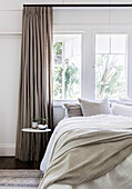 Doppelbett und filigraner Nachttisch vor Fenster mit bodenlangem Vorhang
