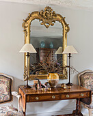 Gilt framed mirror above wooden console with pair of lamps and chairs