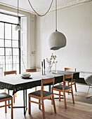 Dining table with grey tablecloth, chairs and pendant lamps in front of window