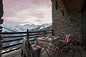 Esstisch mit zwei Stühlen auf Balkon mit Natursteinwand und Blick auf Berglandschaft