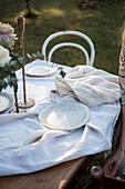 Handmade, cream-coloured plates on pale linen tablecloth in the garden