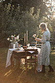 Frau steht am festlich gedeckten Tisch im spätsommerlichen Garten