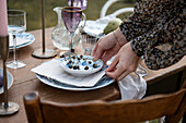 Frauenhände arrangieren blau-weißes Gedeck mit Menükarte auf Holztisch