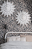 White paper stars on leaf-patterned wallpaper above bed in bedroom